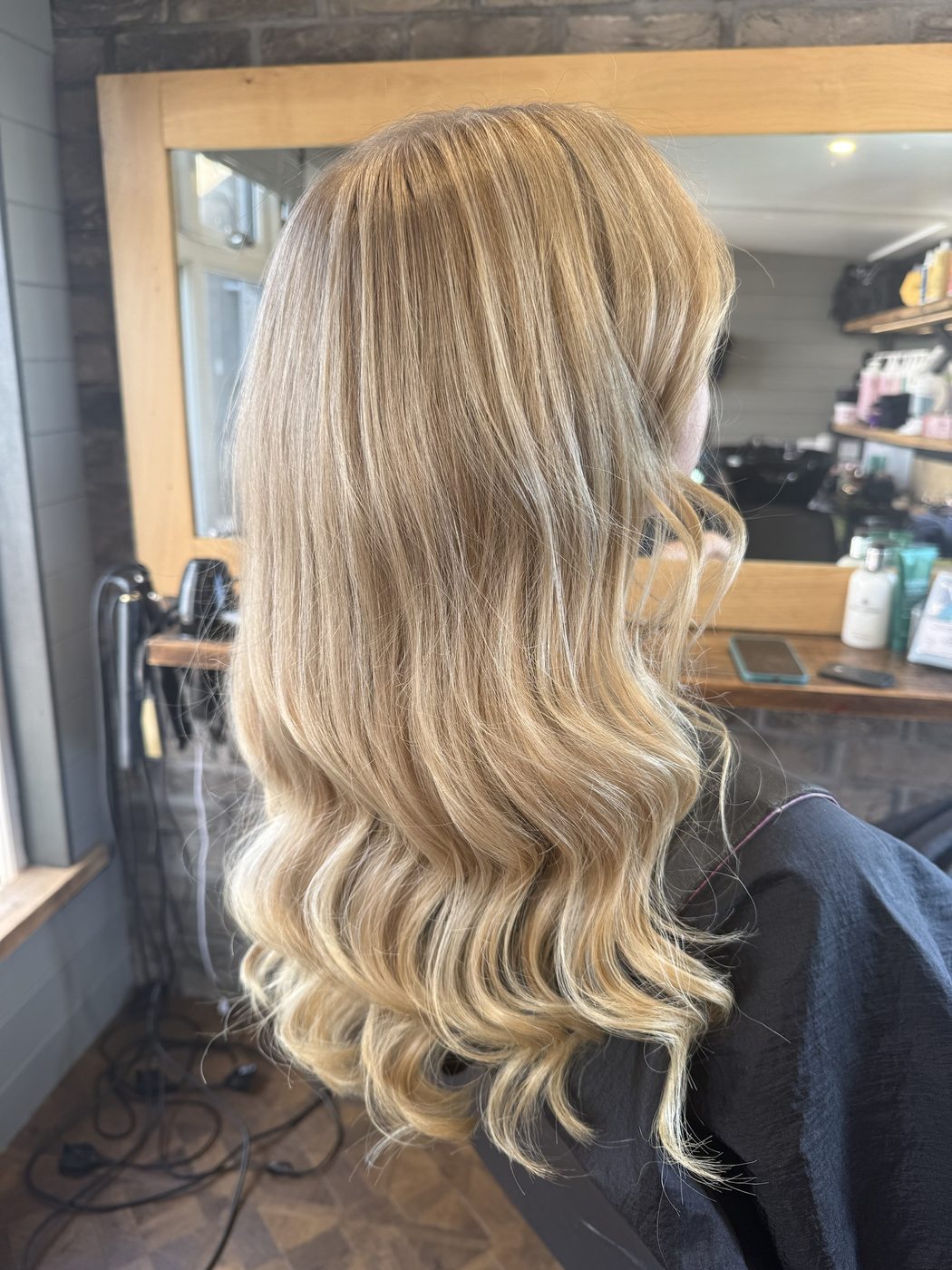 After: flat golden lengths brightened into a soft, dimensional blonde with loose waves