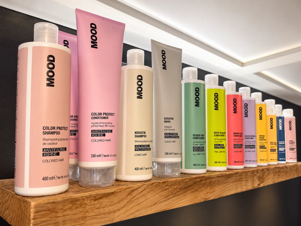 A long wooden shelf at The Hair Room lined with MOOD haircare bottles in soft pinks, creams, greens, yellows, coral and lilac